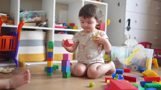 baby plays with blocks on the floor in kindergarten. happy family kid concept. baby girl builds a tower from cubes and plays with toys. development of lifestyle fine motor skills concept