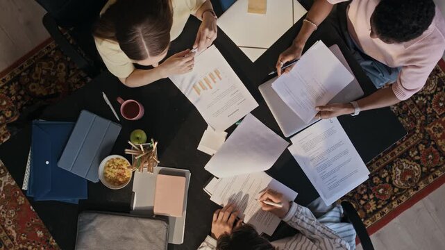 Overhead arc shot of office team analyzing financial graphs and documents during collaborative corporate meeting