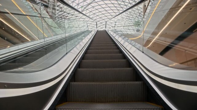 Stab no people shot of empty escalator staircase moving upwards in modern shopping mall interior with geometric glass ceiling