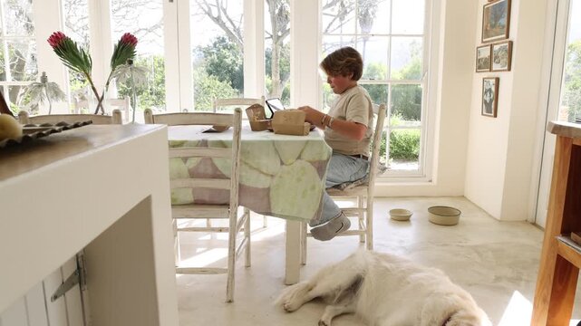 12 year old boy eating box lunch in kitchen using tablet computer