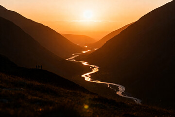 Obraz premium Sunset over winding river in mountainous landscape with hikers silhouette