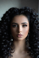 Fototapeta premium A beautiful woman with long, dark, curly hair is posing for a portrait against a plain background.