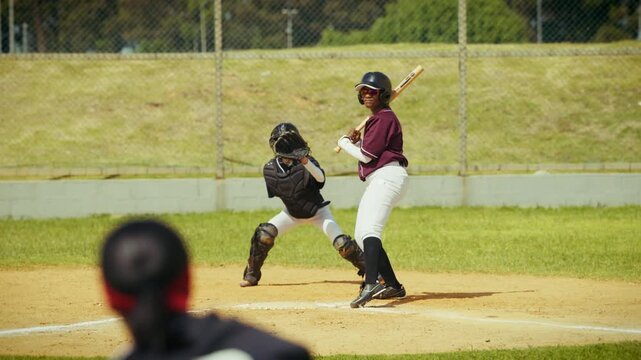 A batter misses a pitch during a baseball game, with the catcher ready behind home plate and the pitcher in the foreground. Intense sports action.