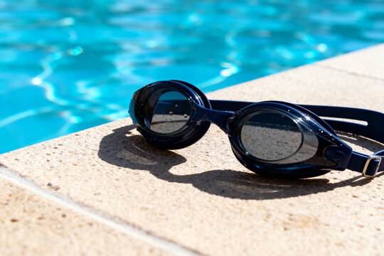 Black Swimming Goggles on Poolside Edge with Clear Blue Water in Background