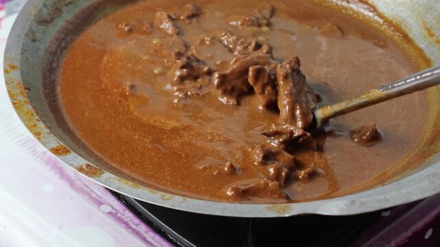 Indonesian beef rendang being stirred and simmered slowly over a gas stove in a large traditional wok with rich spices.