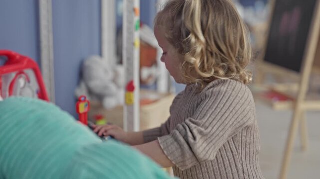 Girl touches toy register with hand while playing at a studio table and pressing colorful buttons; childhood curiosity.