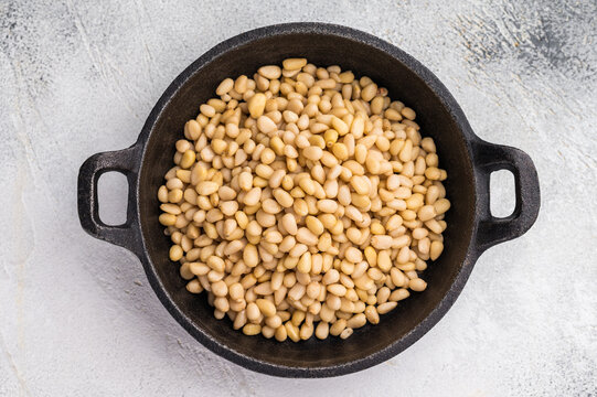 Raw pine nuts arranged in a small cast iron dish on a slate plate over a light textured surface creating a clean contrast for recipe and food visuals