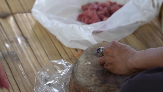 Closeup of a person cutting raw lamb meat with a knife in a metal bowl