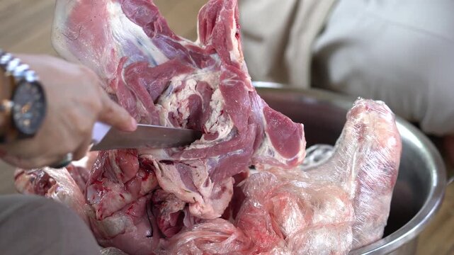 Closeup of a person cutting raw lamb meat with a knife in a metal bowl