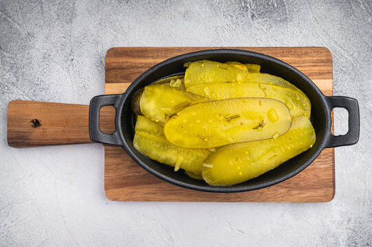 Rustic pickled cucumber slices in cast iron dish with garlic and spices on textured light background, vibrant brined yellow food.
