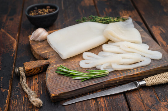 Cleaned squid fillets and rings on textured wood board with rosemary and garlic perfect seafood setup for culinary themes.