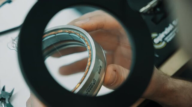 Close-up view of a technician inspecting copper coil windings on a circular electric motor stator through a magnifying lens for precise quality control at the workbench.