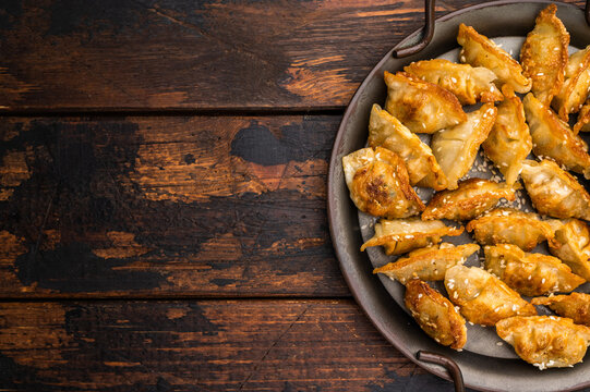 Crispy fried mandu dumplings with sesame dipping sauce on a wooden background. Golden panfried potstickers in a rustic metal plate.