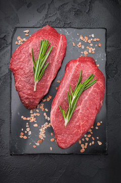 Marbled Wagyu beef chuck top blade steak similar to angus and yakiniku cuts displayed with rosemary on dark textured backdrop great for steakhouse food stock.