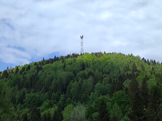 Obraz premium Communication tower on top of a lush green hill under a cloudy sky