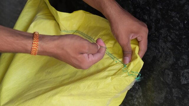 Close-up of hands opening a bag of Urea fertilizer by pulling the stitched thread
