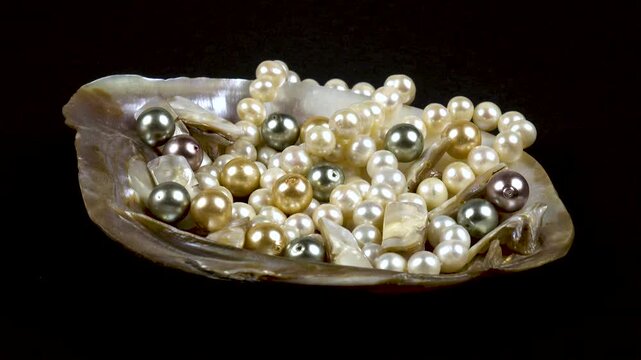 Large mother-of-pearl shell with pearl beads, pieces of pearl and pearl white necklace lying on a black table, side view