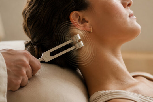 Relaxation and healing are enhanced through somatic therapy as tuning fork is applied near ear of woman receiving treatment