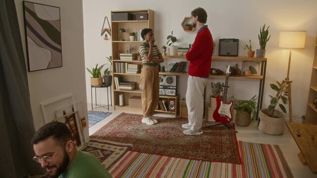 High angle tilt up shot of two friends setting up vynyl record and listening to music while man and woman talking during home party