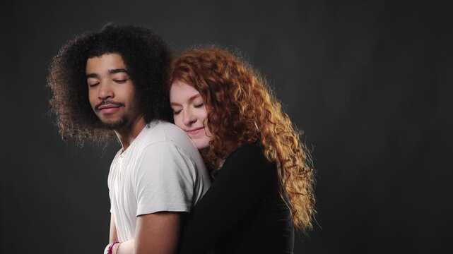This depicts relationship dynamics, showing a young man looking back over his shoulder while a woman leans affectionately on him. The studio portrait captures a moment of intimacy and connection betwe