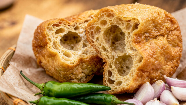 Hollow fried tofu known as tahu pong served with fresh green chilies and garlic cloves in a traditional woven bamboo basket
