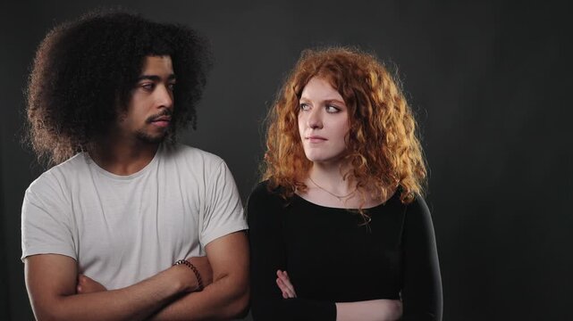 This depicts relationship conflict and misunderstanding, a couple with crossed arms looking away from each other against a dark background. The body language conveys tension, disagreement, and emotion