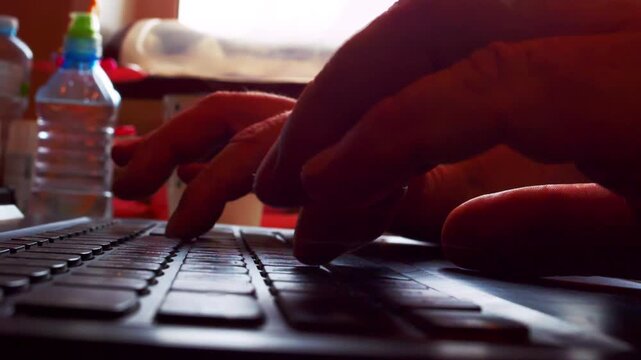 Dynamic time-lapse shot of unrecognized person working on laptop at home office or cafe. Close-up view of fingers typing quickly on keys with soft bokeh and cinematic counter-light from a window.