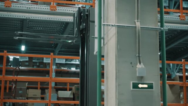 Industrial warehouse interior with tall steel storage racks, pallets of goods, numbered aisles, and a forklift mast, highlighting organized logistics and directional safety signage