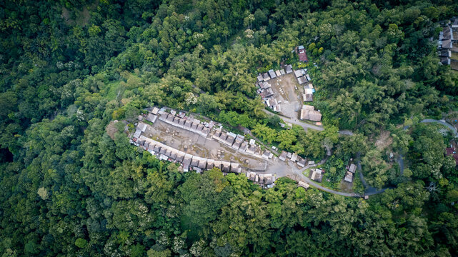 Aerial view of Bena Traditional Village featuring thatched-roof houses arranged in rows surrounded by dense tropical forest in Kecamatan Jerebuu, Nusa Tenggara Timur, Indonesia.