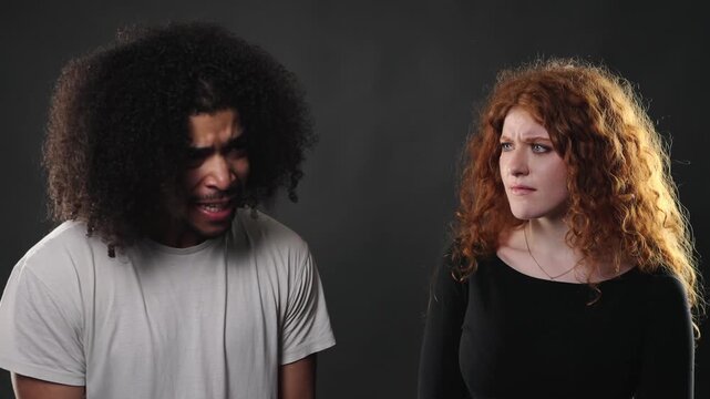 Relationship conflict and misunderstanding are depicted as a young couple argues with disappointed and annoyed expressions. This studio shot captures the emotional tension and communication issues bet