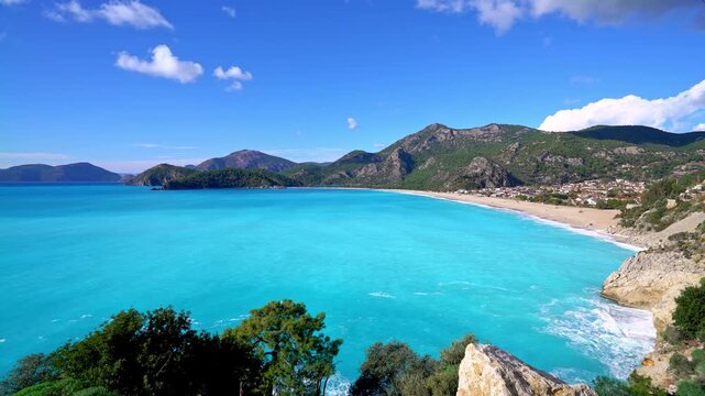 Stunning turquoise beach bay with crystal-clear water, sandy shoreline, and surrounding mountains under a bright blue sky. Scenic coastal panorama ideal for travel and tourism themes.