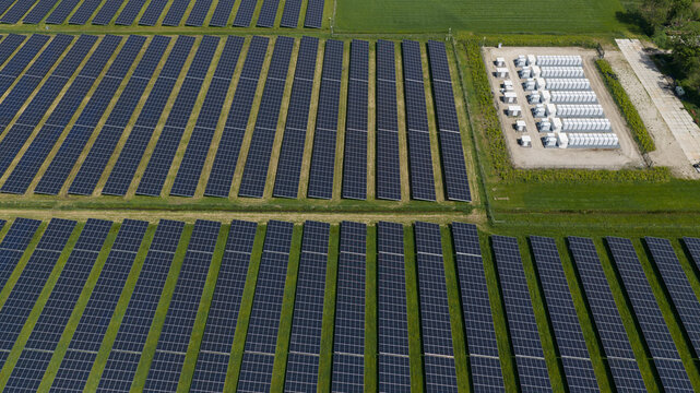 Aerial view of a large solar farm with rows of photovoltaic panels and a battery energy storage system on green fields in Wanneperveen, Overijssel, Netherlands.