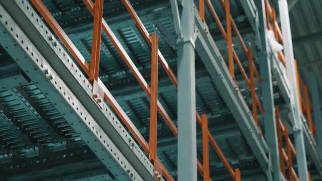 Close-up view of multi-tier industrial warehouse racking with orange safety guardrails and roller conveyors, showing a heavy-duty metal storage structure in a logistics facility