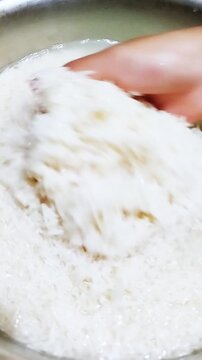 Video of hands washing white rice in water. Rice grains being rinsed and cleaned before cooking. Food preparation, cooking, and culinary concept.