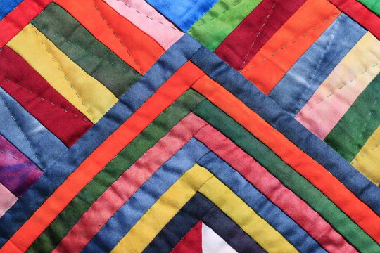 Vibrant strips of hand-dyed cotton fabric create a colorful geometric patchwork quilt pattern
