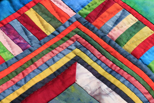 Vibrant strips of hand-dyed cotton fabric create a colorful geometric patchwork quilt pattern