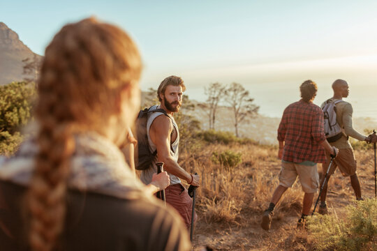 Friends hiking with trekking poles on coastal trail at sunset