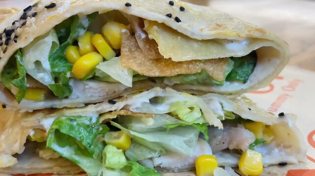 Chinese street food. Closeup sesame flatbread wrap with corn. Layers of crisp lettuce, crunchy fried chip, creamy white sauce, scattered black sesame seeds. 