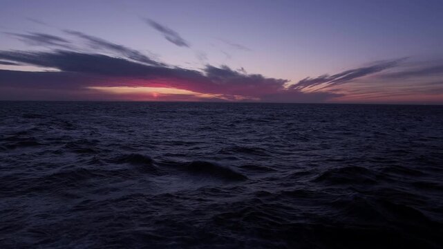 Science of a container cargo ship sailing through a harbor at sunset with a city silhouette in the background.