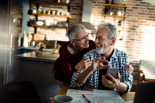 Smiling senior couple paying bills in home kitchen