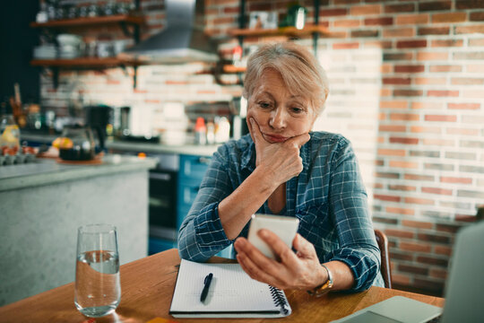 Senior woman looking at smartphone with concern in home kitchen