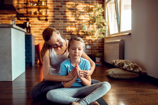 Mother and daughter meditating on yoga mat at home