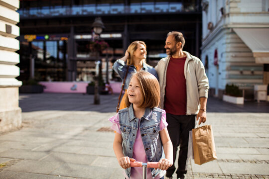 Family with daughter riding scooter on city street