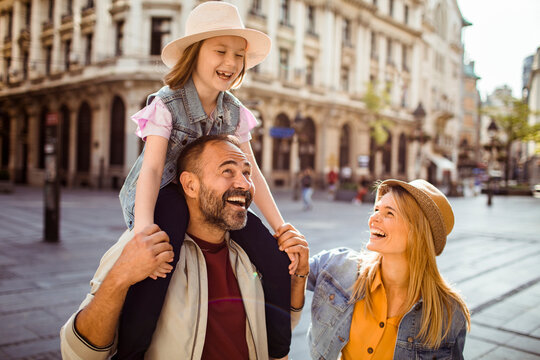 Happy parents carry daughter on shoulders in city street