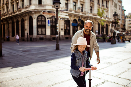 Girl riding scooter with father on sunny city street