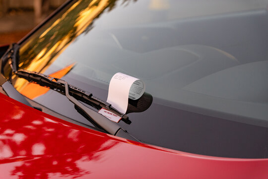 Close up of parking ticket under windshield of red car.