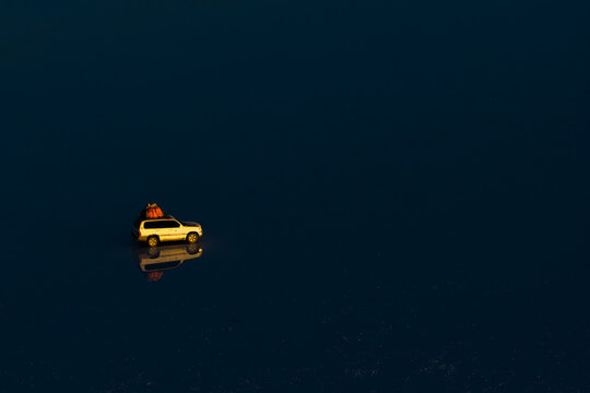 Aerial view of a white SUV with luggage on its roof reflected in the flooded surface of the Uyuni Salt Flat at twilight Potosi Department, Bolivia.