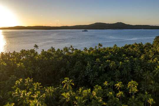 Aerial view of Yasawa Island featuring dense palm tree forests and a boat on the calm ocean water during a golden sunset in Nadi, Western Division, Fiji.