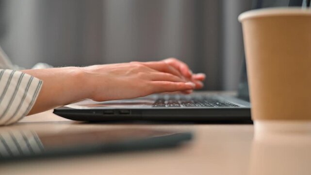 Timelapse person fast typing on a laptop while sitting at a desk in a home office. Their hands are seen actively engaging with both the keyboard and a mobile device, paired with a coffee cup nearby