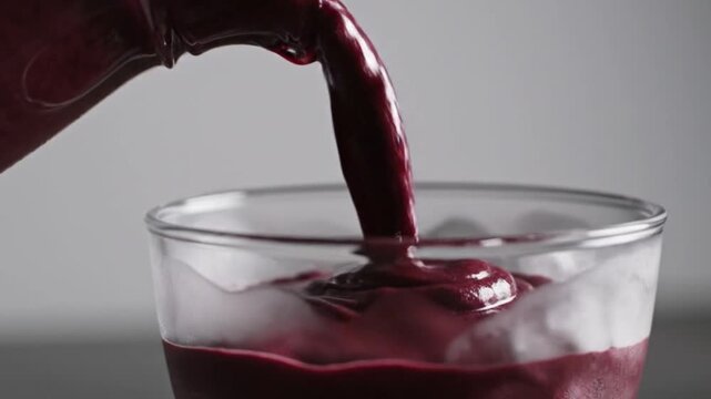 Cinematic close-up of thick cold acai berry pulp being poured into a rustic glass bowl, visible texture, vibrant deep purple color, macro shot, loop
